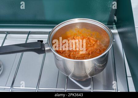 Close-up of cooking chili in a silver pot on an outdoor propane camping stove Stock Photo