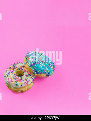 Two donuts with icing and sprinkles on a plain pink background with copy space Stock Photo