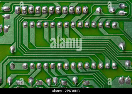 A part of a green printed circuit computer board with tracks. PCB without radio components. Old printed circuit board background with soldering trace, Stock Photo