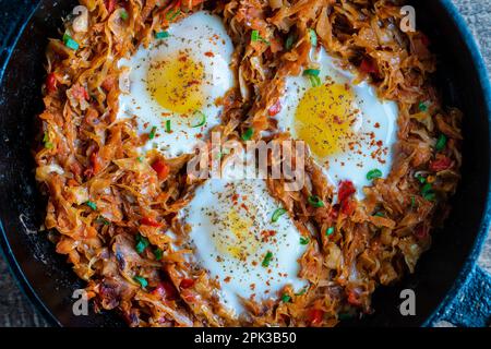 Stewed cabbage with vegetables and fried eggs in a frying pan on a wooden background, close up, top view. Food background. Healthy food Stock Photo