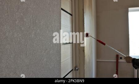 room in the process of renovation, view along the wall at the hands of a painter with a striped roller on a long handle, painting room walls Stock Photo