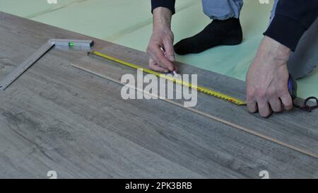 measuring a laminate board with a tape measure in the hands of a worker in a room, putting a mark on a wooden piece of laminate Stock Photo