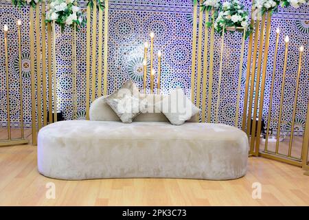 An elegantly staged traditional morocco style wedding with large sofa for the wedding couple to sit and receive blessings from the guests, surrounded Stock Photo
