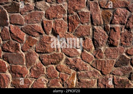 A wall made of rough, red, hewn natural stones. Can be used as a background image. Stock Photo