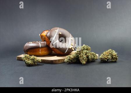 Chocolate-coated donuts lie next to medical marijuana buds.  On a gray background Stock Photo