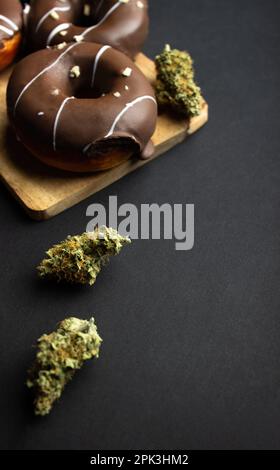 Dry buds of medical marijuana close-up with donuts covered with chocolate icing, sprinkled with nut crumbs.  On a black background Stock Photo