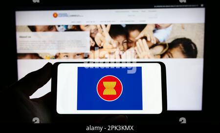 Person holding smartphone with logo of Association of Southeast Asian Nations (ASEAN) on screen in front of website. Focus on phone display. Stock Photo