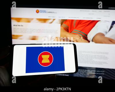Person holding mobile phone with flag of Association of Southeast Asian Nations (ASEAN) on screen in front of web page. Focus on phone display. Stock Photo