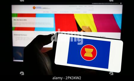 Person holding cellphone with logo of Association of Southeast Asian Nations (ASEAN) on screen in front of webpage. Focus on phone display. Stock Photo