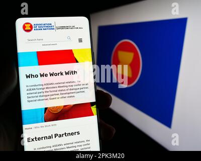 Person holding smartphone with web page of Association of Southeast Asian Nations (ASEAN) on screen with flag. Focus on center of phone display. Stock Photo