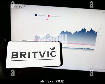 Person holding mobile phone with logo of British soft drinks company Britvic plc on screen in front of business web page. Focus on phone display. Stock Photo