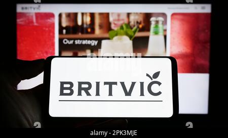 Person holding smartphone with logo of British soft drinks company Britvic plc on screen in front of website. Focus on phone display. Stock Photo