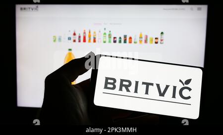 Person holding cellphone with logo of British soft drinks company Britvic plc on screen in front of business webpage. Focus on phone display. Stock Photo