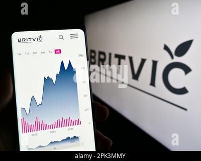 Person holding cellphone with website of British soft drinks company Britvic plc on screen in front of logo. Focus on center of phone display. Stock Photo