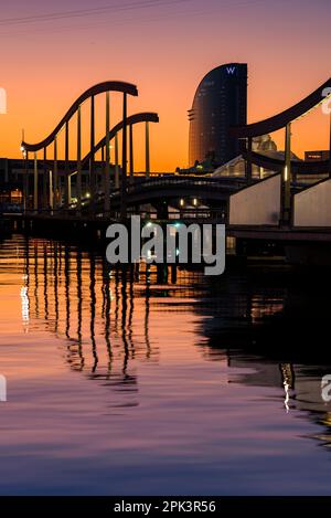 Port Vell (old harbor) of Barcelona and the Hotel W Vela at sunrise, with the calm Mediterranean sea and clear sky (Barcelona, Catalonia, Spain) Stock Photo
