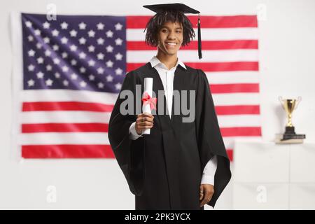 Proud male african american student wearing a graduation gown and holding a diploma in front of the USA flag Stock Photo