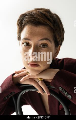 portrait of dreamy freckled woman with short brunette hair looking at camera on grey background,stock image Stock Photo