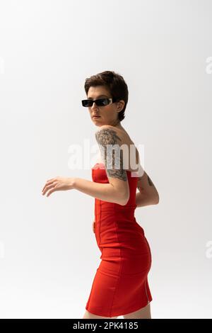 brunette tattooed woman in sunglasses and red corset dress looking at camera isolated on grey,stock image Stock Photo