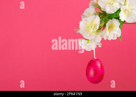 Red easter egg hanging at branch in bloom on vibrant pink background Stock Photo