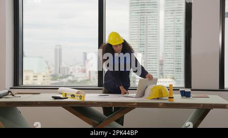 Hardworking female architect with yellow helmet drawing on blueprint Stock Photo