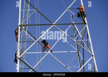 Electricians work overhead to dismantle a high voltage pylon for replacement. Milan, Italy - April 2023 Stock Photo