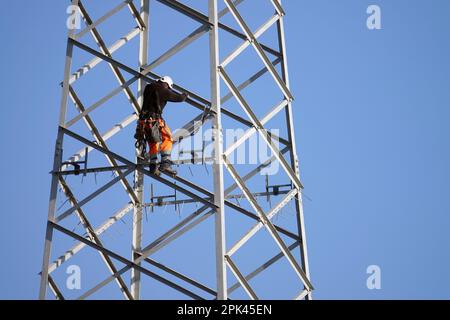 Electricians work overhead to dismantle a high voltage pylon for replacement. Milan, Italy - April 2023 Stock Photo