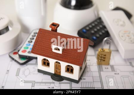 House model, CCTV camera, lock, remote controls, smoke and movement detectors on building plan. Home security system Stock Photo