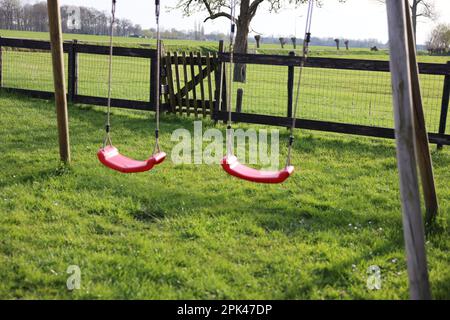 Outdoor swings on green grass near wooden fence outdoors Stock Photo