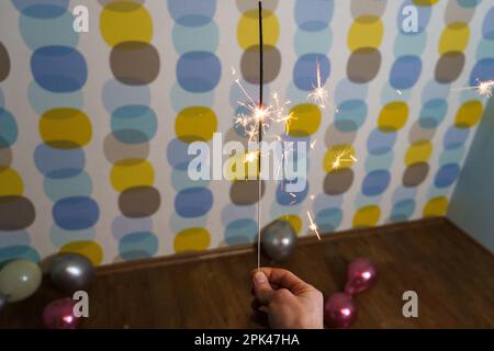 Young Man Holding a Sparkler with Balloons in the Background Stock Photo