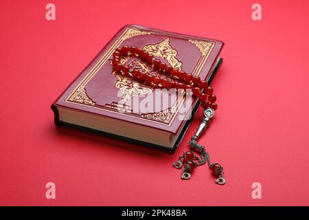 Muslim prayer beads and Quran on red background Stock Photo