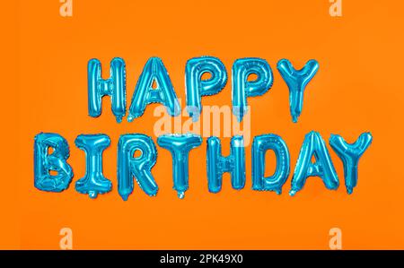 Phrase HAPPY BIRTHDAY made of blue foil balloon letters on orange background Stock Photo