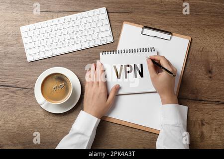 Woman writing acronym VPN in notebook at wooden table, top view. Secure network connection Stock Photo