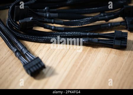Tangled black computer cables lying on a brown wooden table Stock Photo
