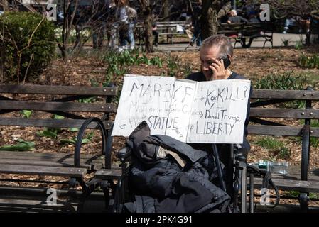 A man sits on a bench outside the arraignment of former president Donald Trump holding a sign asking 'Marry, F**k or Kill? Marjorie Taylor Green, Donald Trump or the Statue of Liberty' Stock Photo
