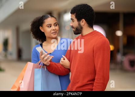 Mixed Spouses Using Mobile Shopping Application On Phone In Mall Stock Photo