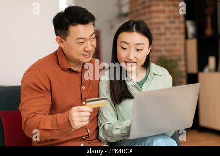 Asian family shopping online from home, using laptop and credit card, purchasing in store or ordering food on Internet Stock Photo