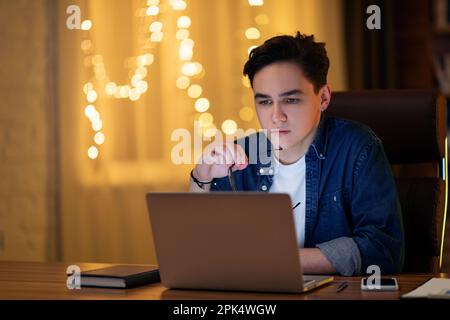 Pensive young caucasian guy developer working on laptop Stock Photo