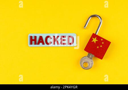 On a yellow surface, an open lock with the image of the flag of China and a sticker with the inscription - hacked Stock Photo
