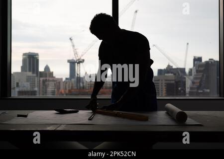 Worker with drawing on blueprint of architectural project plan on building site Stock Photo