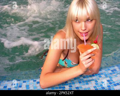 young beautiful woman relaxing in the swimming pool with cocktail Stock Photo