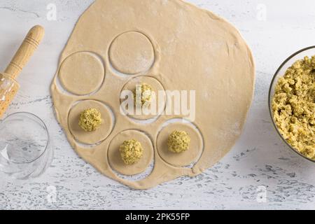 Cooking homemade vegan dumplings, vareniki, pierogi, kreplach  stuffed with vegan lentil "meat", carrots, onions, herbs and spices on light gray textu Stock Photo