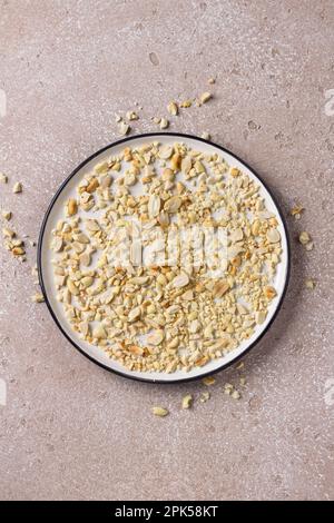 White plate with ground roasted peanuts on beige stone background, flat lay Stock Photo