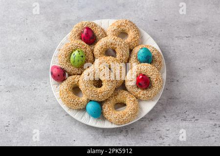 White plate with traditional Greek Easter cookies Koulourakya or Koulourya shortbread rings with sesame seeds, decorated with colored eggs on a gray t Stock Photo