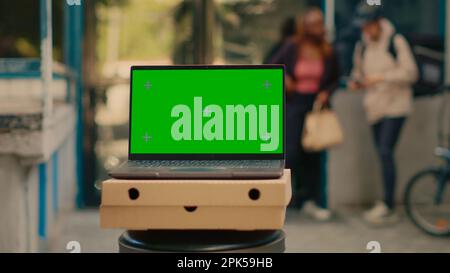 Laptop advertising greenscreen template outside, food delivery service at front door. Running isolated chroma key display with blank mockup and copyspace background on computer screen. Stock Photo