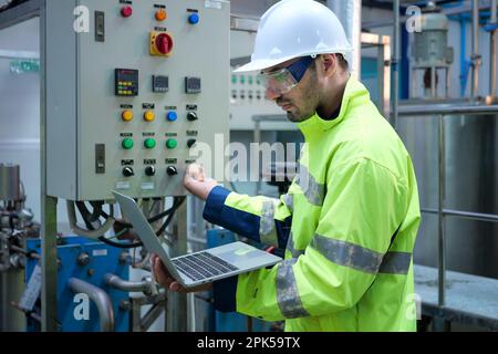 Engineer specialist using laptop checking and maintaining machine in factory Stock Photo