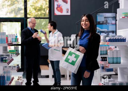 Satisfied pharmacy store client holding prescription medicine purchase bag and looking at camera. Smiling happy buyer holding drugstore paper package with medicaments portrait Stock Photo