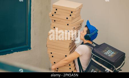 Clumsy food courier trying to catch falling pizza boxes, acting scared and running from client front door after dropping fastfood delivery meal. Afraid carrier with bad service. Handheld shot. Stock Photo