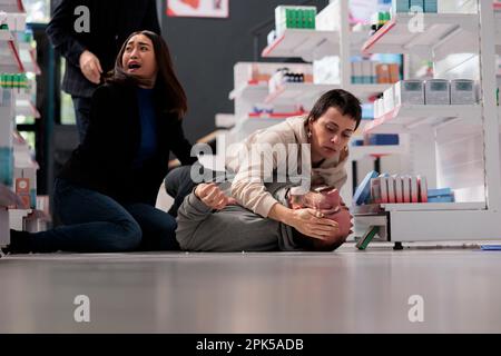 Pharmacy stores buyers rushing to help man with epileptic seizure. Scared asian woman calling drugstore medical workers in panic and giving first aid to person suffering from epilepsy Stock Photo