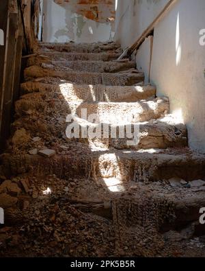Color Image of Low Angle Looking Up Abandoned and Dilapidated Carpet Staircase with Warm Sun Beams Shining Through Exposed Ceiling after Disaster Stock Photo