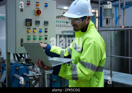 Engineer specialist using laptop checking and maintaining machine in factory Stock Photo